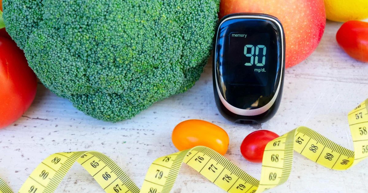 A blood glucose meter reads 90 mg_dL during Continuous Glucose Monitoring in Medford, OR, on a table with fruits, vegetables, and a measuring tape.